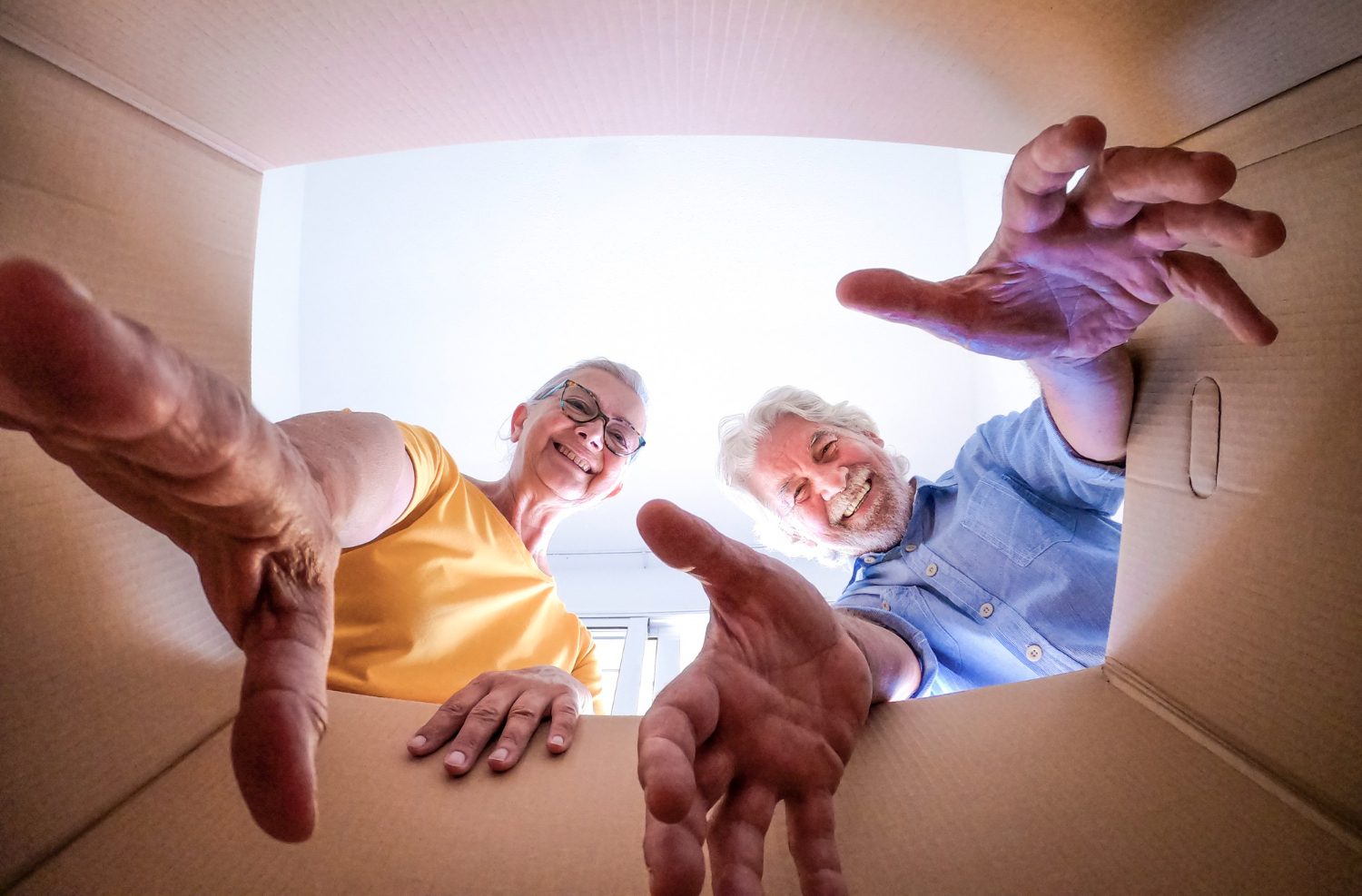 bottom-view-couple-smiling-elderly-people-moving-house-opening-packing-boxes